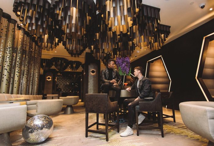 Gay-friendly W New York Times Square Hotel bar. Two men enjoy cocktails under a modern chandelier. Disco ball on the floor. NYC gay travel.