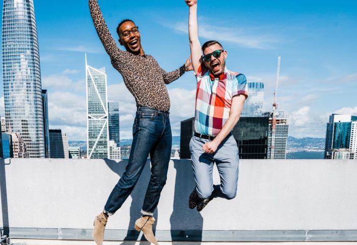 Two gay men jumping for joy at W San Francisco hotel. Celebrating LGBTQ travel in a gay-friendly hotel with city skyline view.