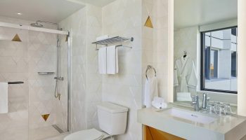 W San Francisco gay-friendly hotel bathroom. Shower, toilet, sink, and mirror. Modern design with white and gold accents. Gay travel advice.