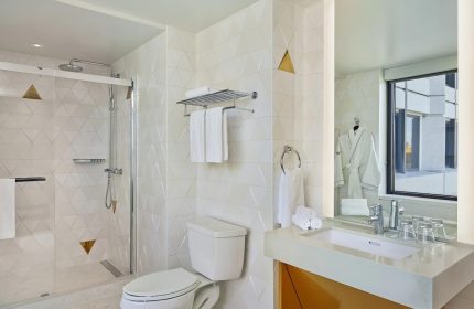 W San Francisco gay-friendly hotel bathroom. Shower, toilet, sink, and mirror. Modern design with white and gold accents. Gay travel advice.