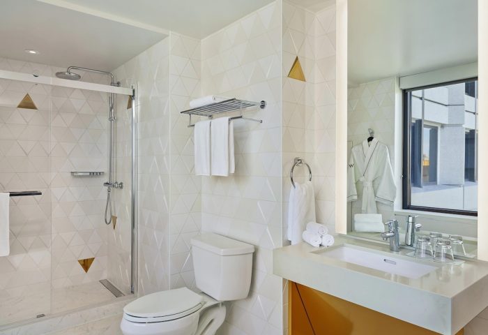 W San Francisco gay-friendly hotel bathroom. Shower, toilet, sink, and mirror. Modern design with white and gold accents. Gay travel advice.