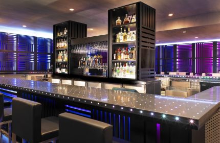 Bar at W San Francisco, a gay-friendly hotel. Modern design with liquor shelves, glasses, and beer taps. Blue and purple lighting.