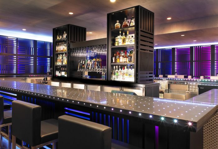 Bar at W San Francisco, a gay-friendly hotel. Modern design with liquor shelves, glasses, and beer taps. Blue and purple lighting.