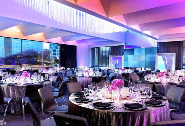 W San Francisco hotel ballroom setup for a gay wedding. Tables with flowers, glasses, and black napkins fill the room. Purple lighting.