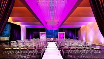 W San Francisco, a gay-friendly hotel: Wedding venue with chairs lining a white aisle. The room is lit with purple lights. Elegant and modern.