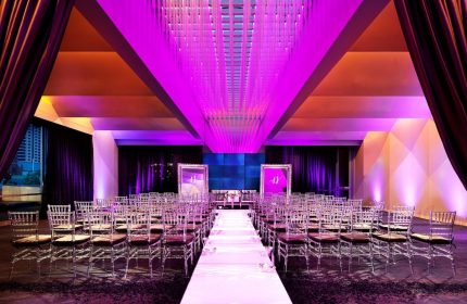 W San Francisco, a gay-friendly hotel: Wedding venue with chairs lining a white aisle. The room is lit with purple lights. Elegant and modern.