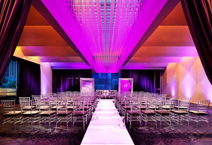 W San Francisco, a gay-friendly hotel: Wedding venue with chairs lining a white aisle. The room is lit with purple lights. Elegant and modern.