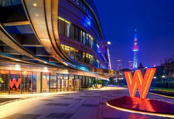 W Shanghai - The Bund at night. Gay-friendly hotel exterior view with the Oriental Pearl Tower in the background. Shanghai travel for gay men.