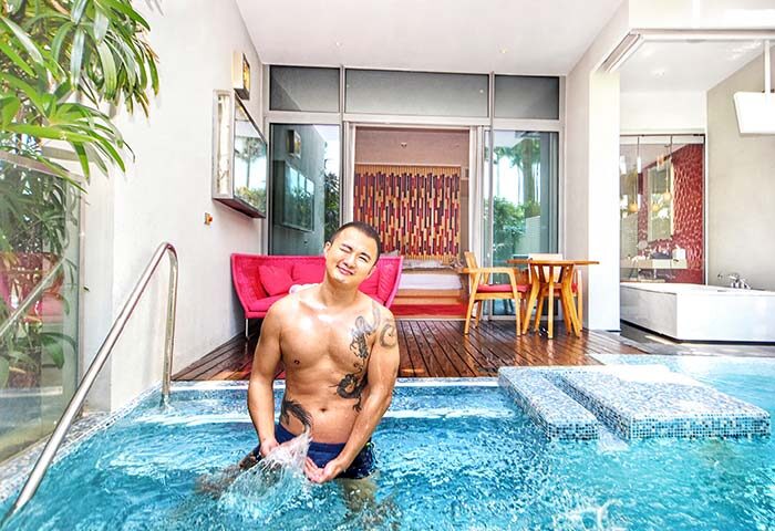 Gay man at W Singapore - Sentosa Cove, a gay-friendly hotel. He's in the pool of his SG Clean Certified room, smiling for the camera.
