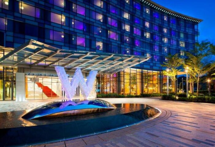 W Singapore - Sentosa Cove entrance at dusk. Gay-friendly hotel with SG Clean Certified. Modern architecture, water feature, and illuminated 'W' logo.