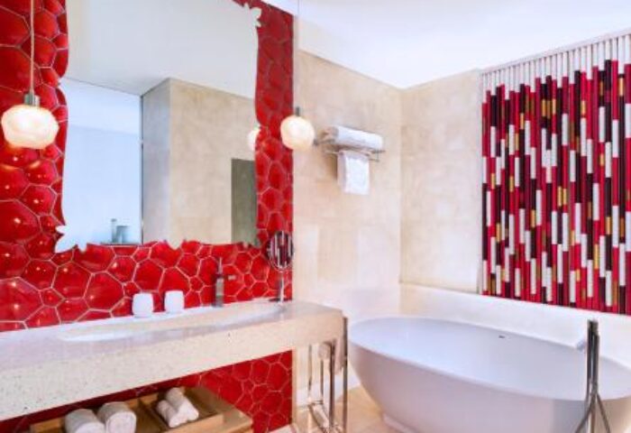 W Singapore Sentosa Cove's bathroom. Red honeycomb tiles surround a large mirror. A modern bathtub is visible. Gay-friendly hotel.