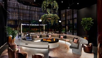 W Toronto, a gay-friendly hotel. Modern lounge area with a fire pit, curved seating, and lush greenery. Upscale interior design.