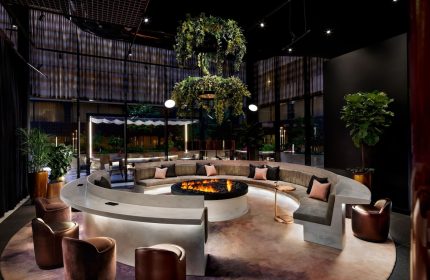 W Toronto, a gay-friendly hotel. Modern lounge area with a fire pit, curved seating, and lush greenery. Upscale interior design.