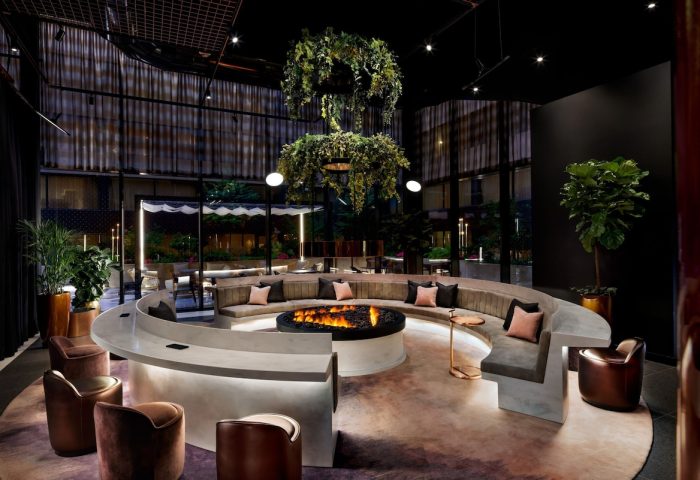 W Toronto, a gay-friendly hotel. Modern lounge area with a fire pit, curved seating, and lush greenery. Upscale interior design.