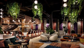 Interior of W Toronto, a gay-friendly hotel. Bar with stools, hanging plants, lounge area with plush seating, and modern lighting. Upscale.