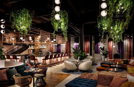 Interior of W Toronto, a gay-friendly hotel. Bar with stools, hanging plants, lounge area with plush seating, and modern lighting. Upscale.
