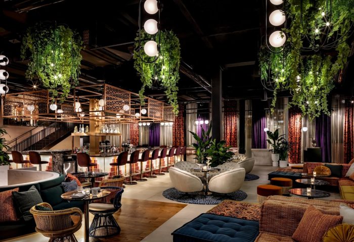 Interior of W Toronto, a gay-friendly hotel. Bar with stools, hanging plants, lounge area with plush seating, and modern lighting. Upscale.