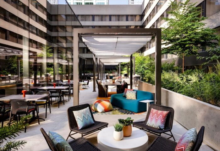 Outdoor patio at W Toronto, a gay-friendly hotel. Tables, chairs, and lounge seating under a pergola. Greenery surrounds the space.