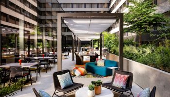 Outdoor patio at W Toronto, a gay-friendly hotel. Tables, chairs, and lounge seating under a pergola. Greenery surrounds the space.