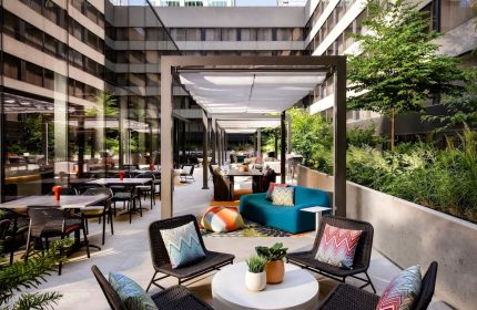 Outdoor patio at W Toronto, a gay-friendly hotel. Tables, chairs, and lounge seating under a pergola. Greenery surrounds the space.