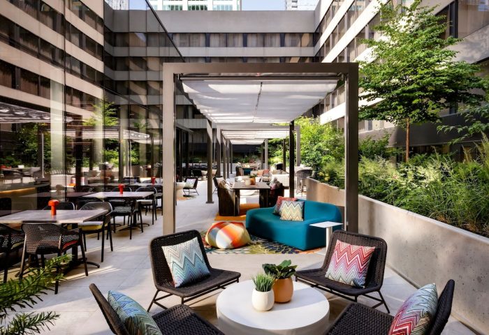 Outdoor patio at W Toronto, a gay-friendly hotel. Tables, chairs, and lounge seating under a pergola. Greenery surrounds the space.