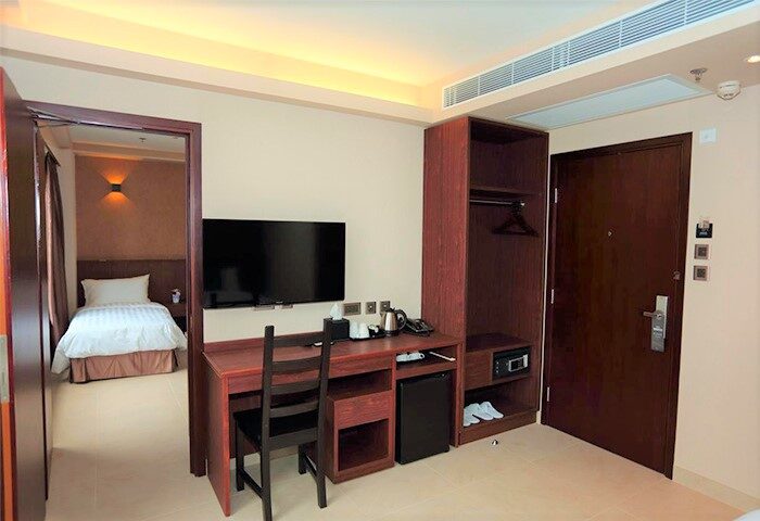 WE Hotel room interior. Gay-friendly hotel with desk, tv, closet, and view into a second room with a bed. Modern design.