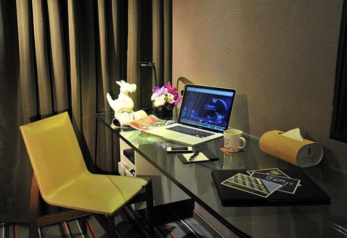 WESTGATE Hotel's gay-friendly room: Desk with laptop, chair, flowers, and dragon statue. Ideal for gay men's travel, offering comfort & style.