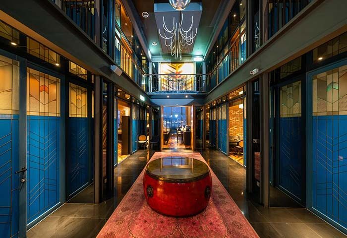 WOLO Kuala Lumpur gay-friendly hotel interior. Hallway view with blue doors, a red drum table on a pink rug, and a modern chandelier.
