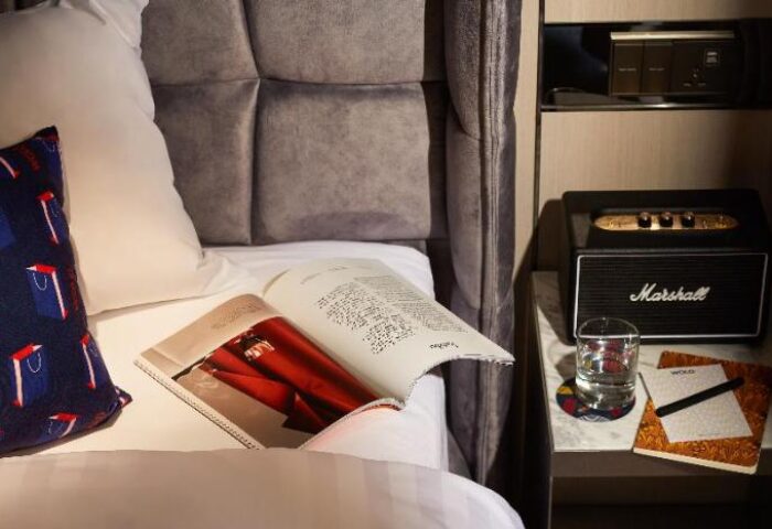 WOLO Kuala Lumpur hotel room detail. Bedside table with Marshall speaker, glass of water, and WOLO-branded notepad. Gay-friendly hotel.