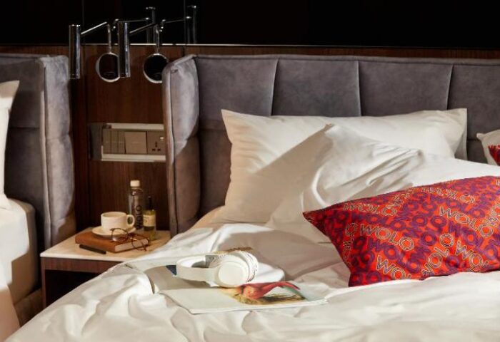 WOLO Kuala Lumpur gay-friendly hotel room. Bed with white sheets, WOLO pillow, headphones, and bedside table with a cup and glasses.