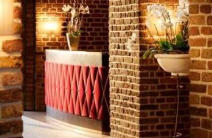 Interior of Wasserturm Hotel Cologne, a gay-friendly Curio Collection by Hilton. Brick walls and a red reception desk with flower decorations.