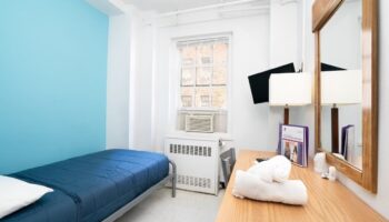 West Side YMCA Hostel room. Budget gay-friendly hotel with single bed, desk, mirror, TV, and air conditioner. Clean, simple lodging.