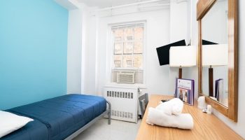 West Side YMCA Hostel room. Budget gay-friendly hotel with single bed, desk, mirror, TV, and air conditioner. Clean, simple lodging.