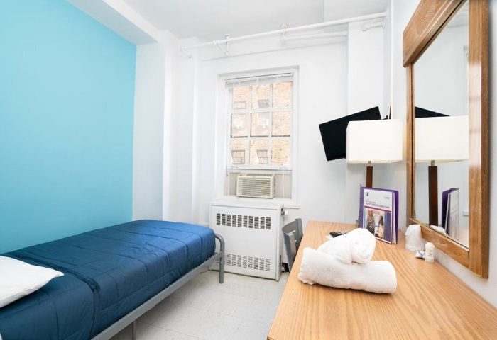 West Side YMCA Hostel room. Budget gay-friendly hotel with single bed, desk, mirror, TV, and air conditioner. Clean, simple lodging.