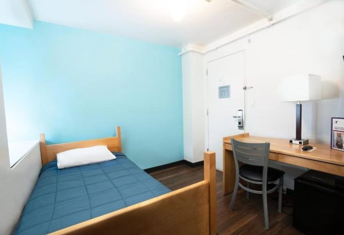 West Side YMCA Hostel room. Gay-friendly hotel with single bed, desk, chair, and blue accent wall. Budget-friendly lodging for gay travelers.