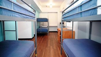 Dorm room interior at West Side YMCA Hostel, a gay-friendly hotel. Bunk beds with blue bedding, wooden floor, desks. Budget travel.