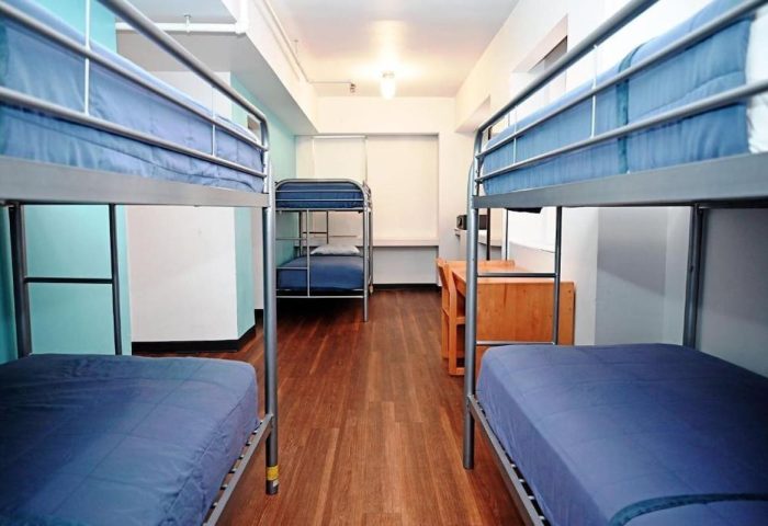 Dorm room interior at West Side YMCA Hostel, a gay-friendly hotel. Bunk beds with blue bedding, wooden floor, desks. Budget travel.