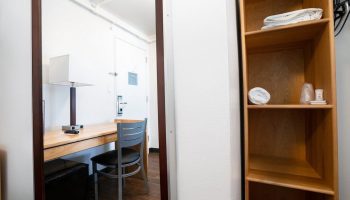 West Side YMCA Hostel room. Desk, chair, lamp reflected in mirror. Shelves with towels. Gay-friendly hotel for gay men travelers.