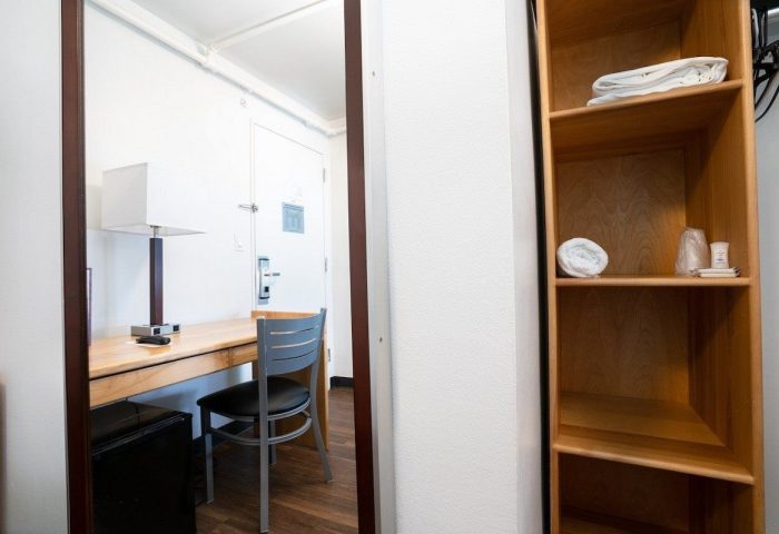 West Side YMCA Hostel room. Desk, chair, lamp reflected in mirror. Shelves with towels. Gay-friendly hotel for gay men travelers.