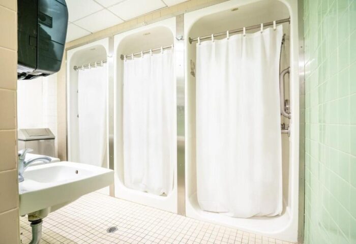 West Side YMCA Hostel showers. Interior of a gay-friendly hotel bathroom with shower stalls and a sink. Budget travel for gay men.