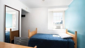 West Side YMCA Hostel room. Gay-friendly hotel with a bed, desk, chair, mirror, and window. Great for gay men's travel to NYC.