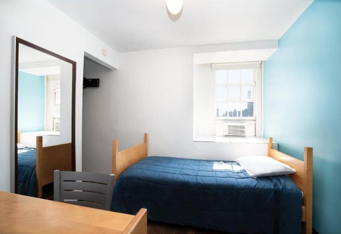 West Side YMCA Hostel room. Gay-friendly hotel with a bed, desk, chair, mirror, and window. Great for gay men's travel to NYC.