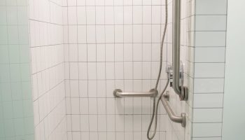 West Side YMCA Hostel gay-friendly hotel shower. Accessible bathroom with grab bars. Modern white tile design. Clean and well-lit.