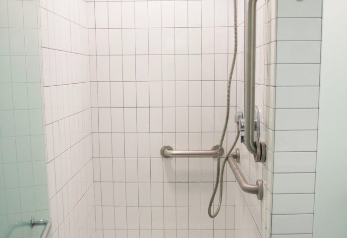 West Side YMCA Hostel gay-friendly hotel shower. Accessible bathroom with grab bars. Modern white tile design. Clean and well-lit.