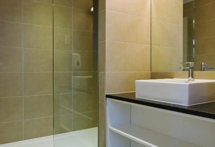 Bathroom at Wombats City Hostel London, a gay-friendly hotel. Features a shower, sink, mirror, and storage. Clean and modern design.