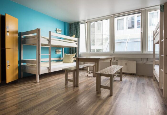 Wombats City Hostel Munich dorm room. Bunk beds, table, and benches in a bright, clean space. A gay-friendly hotel for travelers.