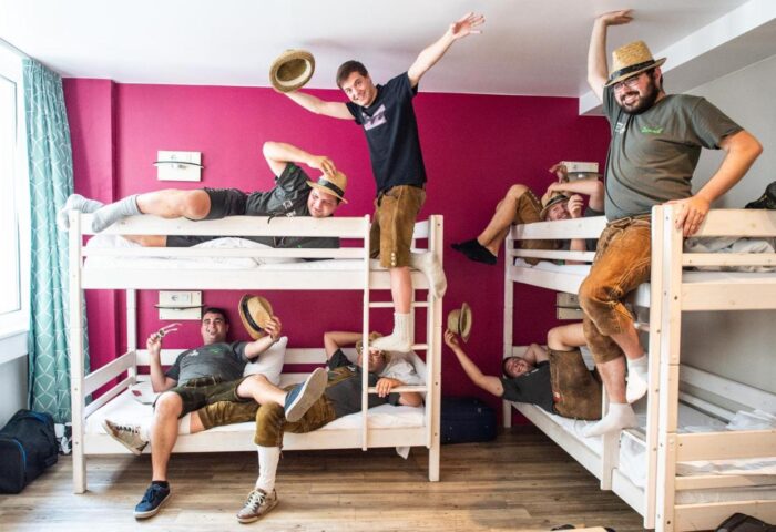 Wombats City Hostel Munich gay-friendly dorm: Group of men in lederhosen and hats having fun on bunk beds. Gay travel advice.