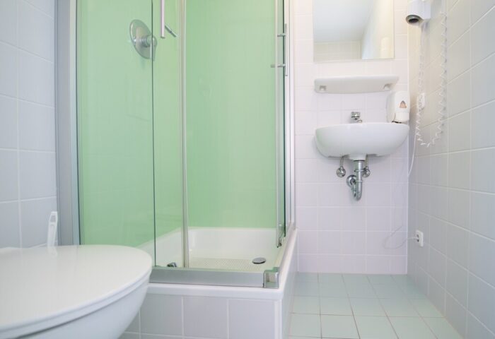 Bathroom at Wombats City Hostel Munich, a gay-friendly hotel. Features include a shower, sink, toilet, and hairdryer. Clean, tiled interior.
