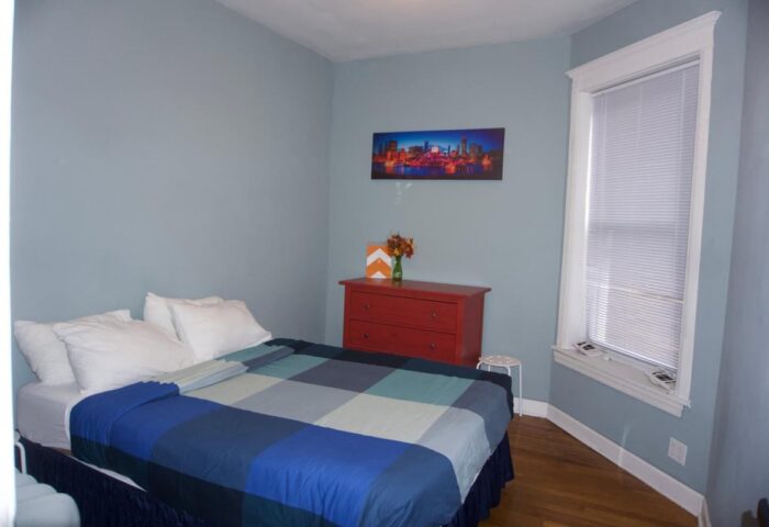 Bedroom at Wrigley Hostel, an adults-only, gay-friendly hotel. Features a bed, dresser, and city skyline art. Great for gay travel.