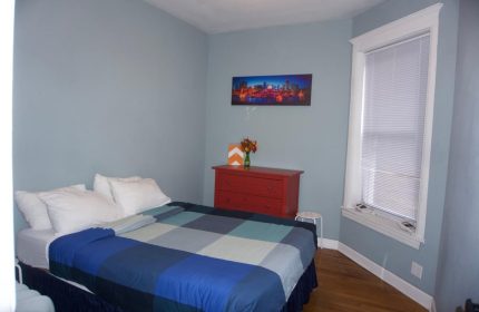 Bedroom at Wrigley Hostel, an adults-only, gay-friendly hotel. Features a bed, dresser, and city skyline art. Great for gay travel.
